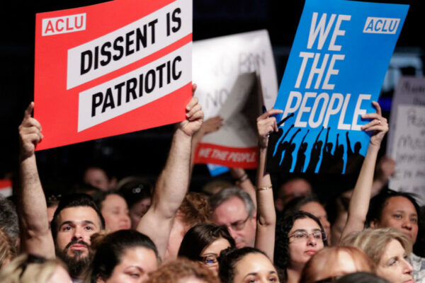 protestors holding signs that say we the people, dissent is patriotic