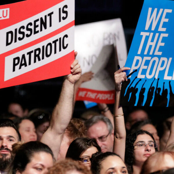 protestors holding signs that say we the people, dissent is patriotic