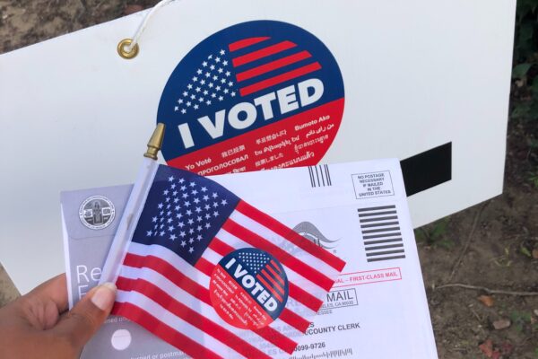 Person holding flag and sign that says "I voted"
