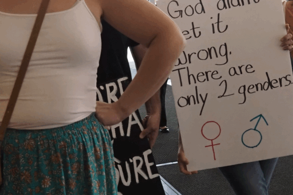 Halsey Yankey stands in front of a protester at a gender marker clinic held at the Lawrence Public Library on May 17, blocking his transphobic sign from view. (Rachel Mipro/Kansas Reflector)