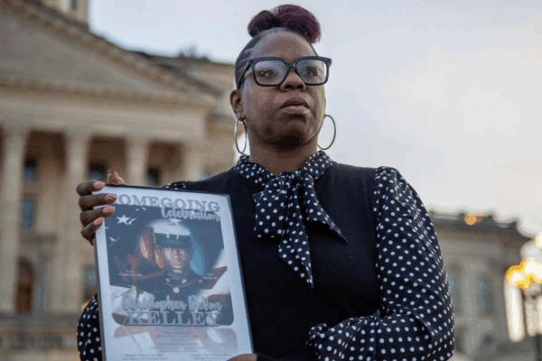 Christian Kelley showcases a framed photo of her brother Christopher DeVon Kelley in front of the Kansas Statehouse in Topeka. Officers shot and killed the Marine Corps veteran in June 2022. Emily Curiel