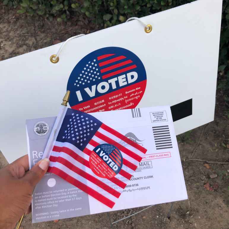 Person holding flag and sign that says "I voted"