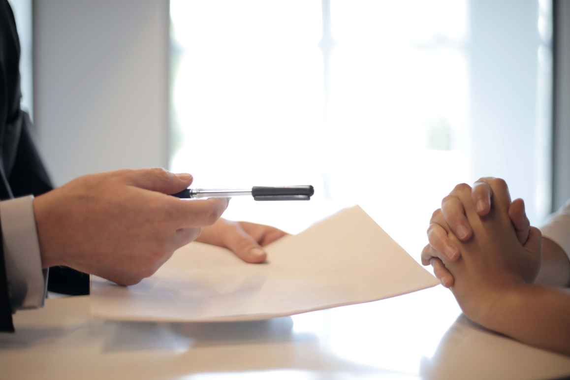 Man holding pen and legal paper out for someone