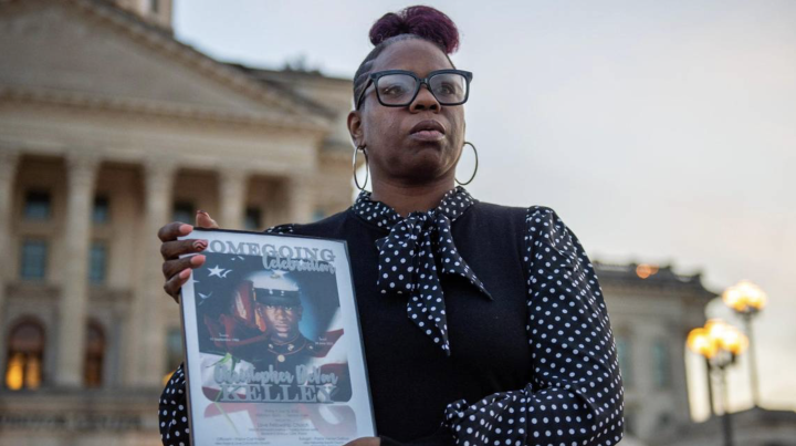 Christian Kelley showcases a framed photo of her brother Christopher DeVon Kelley in front of the Kansas Statehouse in Topeka. Officers shot and killed the Marine Corps veteran in June 2022. Emily Curiel