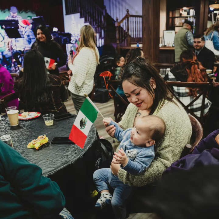 Noi Siriphone, an immigrant from Laos, and her partner, Ivan Morales, an immigrant from Mexico, laugh as their 9-month-old son, Zayne Morales, plays with a Mexican flag during a traditional holiday celebration in early December. (Meridith Kohut for The Wa