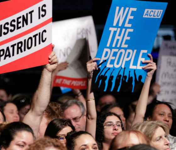 protestors holding signs that say we the people, dissent is patriotic